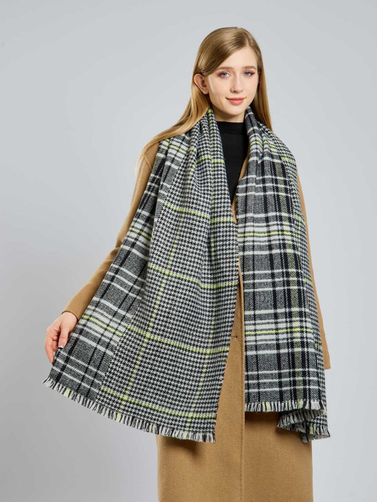 Woman in a tan coat holding her large houndstooth and plaid scarf