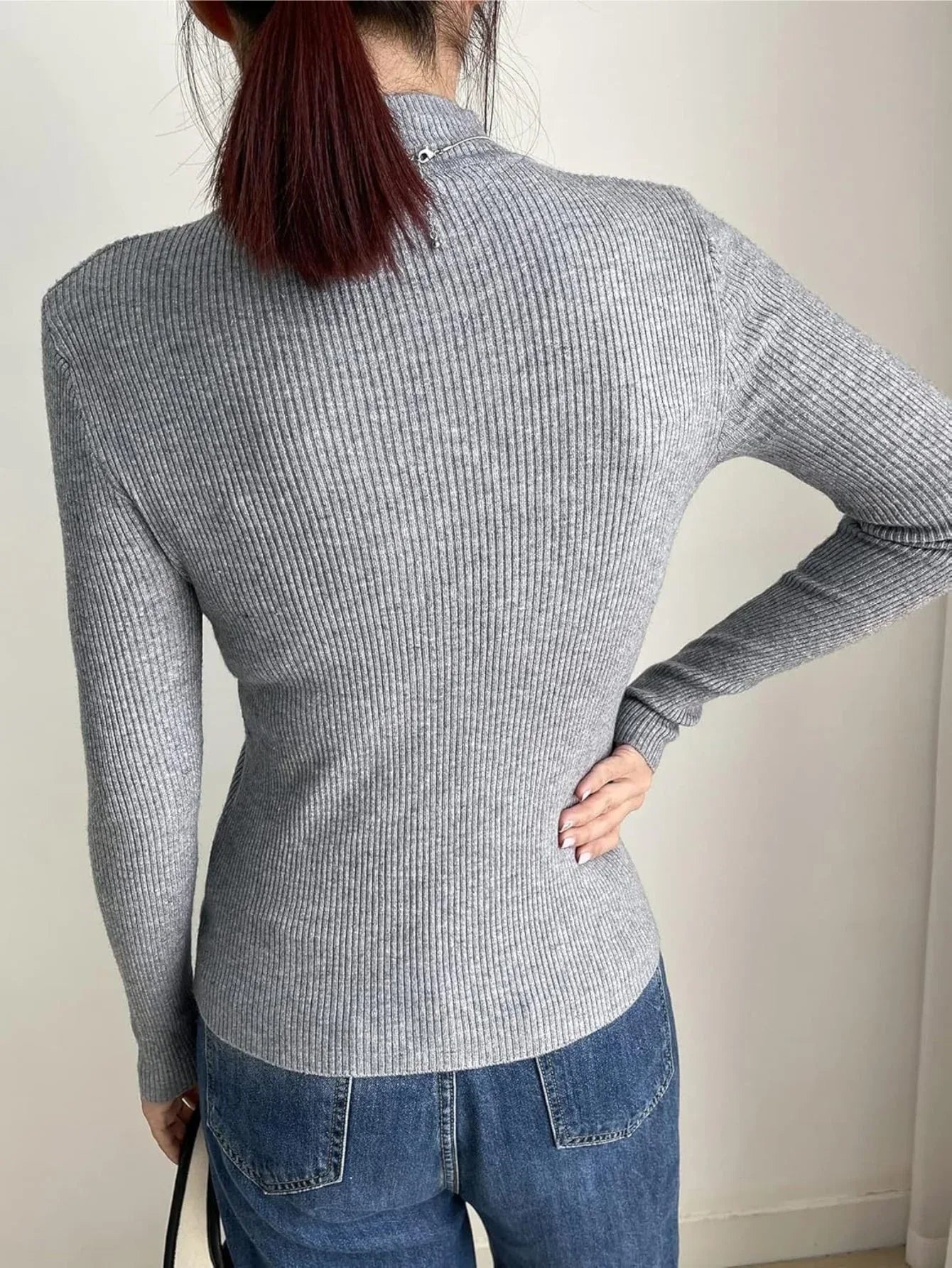 Back view of a woman wearing a gray ribbed mock neck long sleeve sweater and blue jeans
