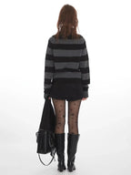 Back view of a model wearing a grey and black striped sweater with a turtleneck, black shorts, black tights with stars, and black boots, holding a black bag.
