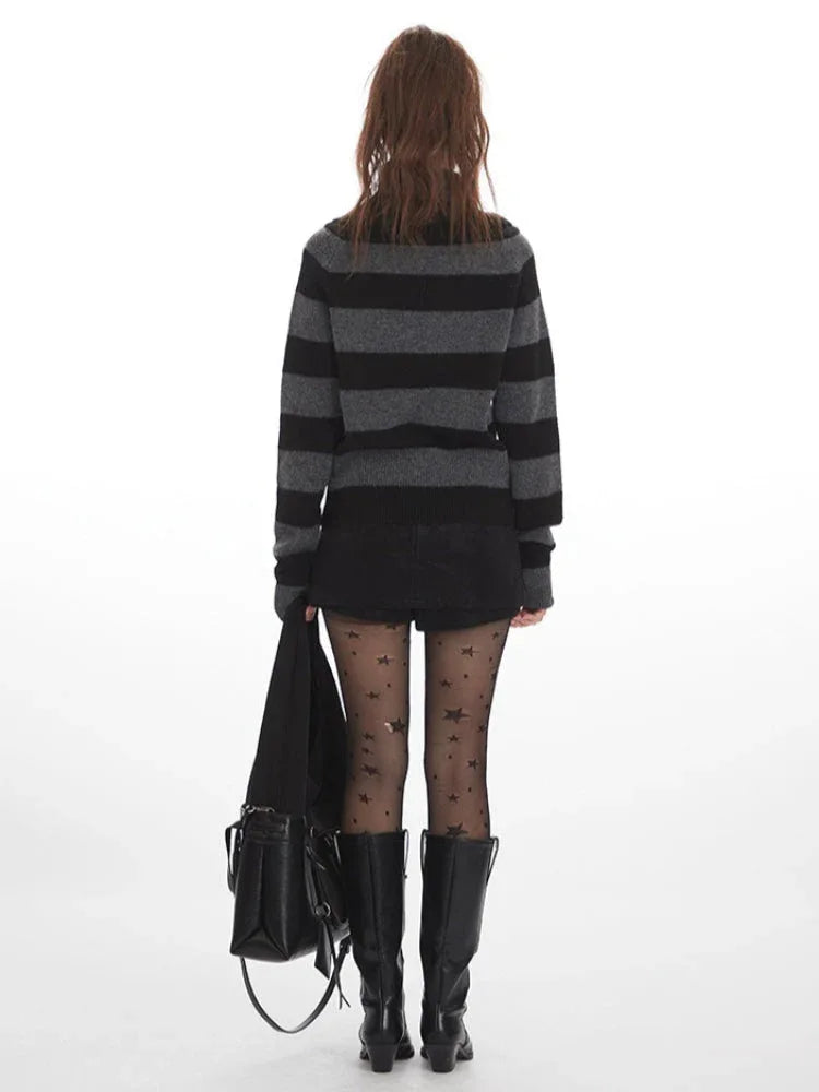 Back view of a model wearing a grey and black striped sweater with a turtleneck, black shorts, black tights with stars, and black boots, holding a black bag.