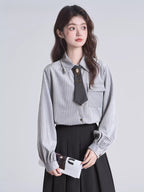Woman in a grey pinstripe shirt and black pleated skirt, holding a folded magazine.