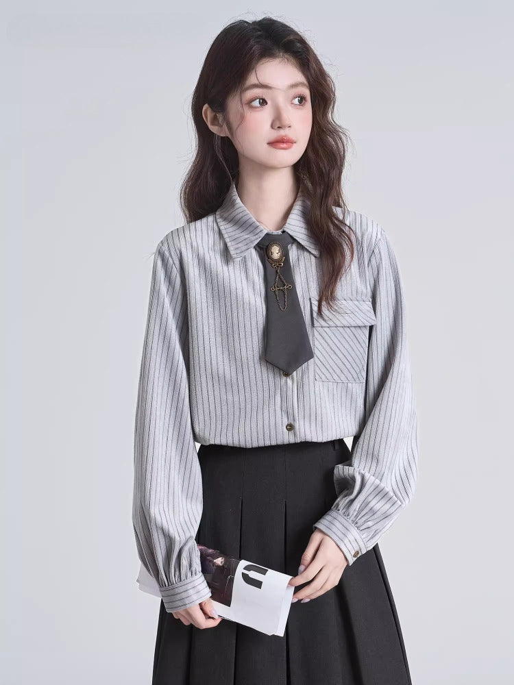 Woman in a grey pinstripe shirt and black pleated skirt, holding a folded magazine.