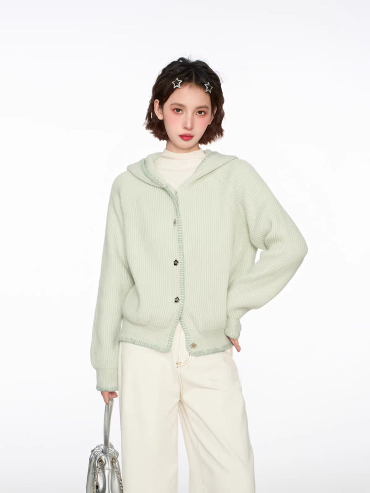 Woman wearing a light green hooded cardigan with white pants and a silver bag, front view