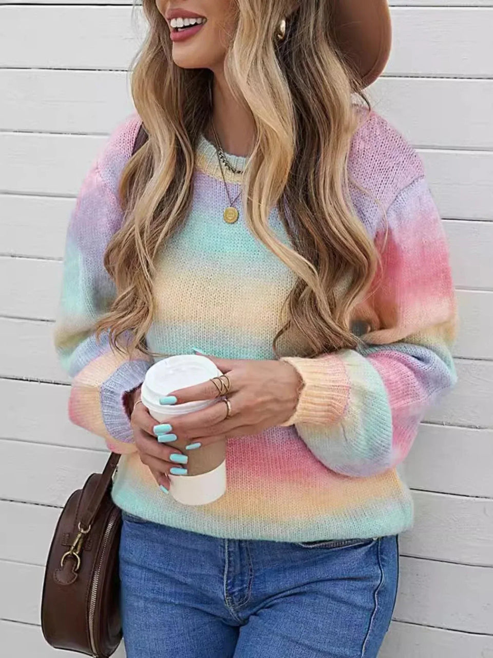 Woman wearing a rainbow gradient knit sweater with blue jeans, holding a coffee cup. Main image