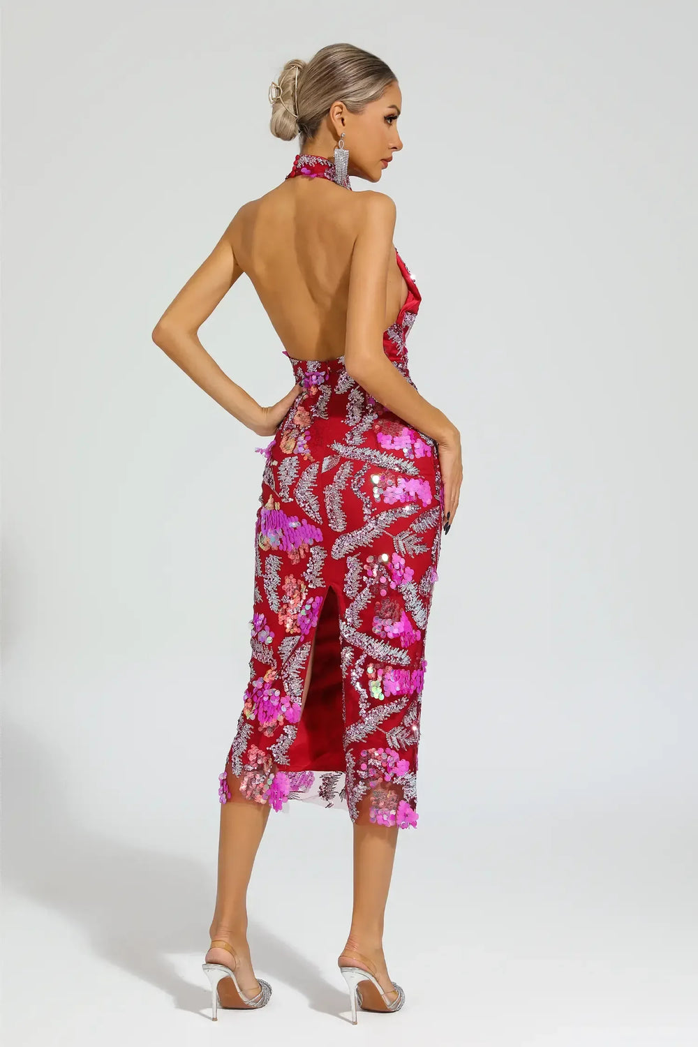 Rear view of a woman in a red sequined halter midi dress with floral appliques and an open back.