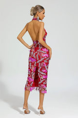 Rear view of a woman in a red sequined halter midi dress with floral appliques and an open back.