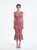 Woman wearing a pink lace dress with ruffled cap sleeves and a mermaid hemline, front view.