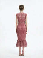Woman wearing a pink lace dress with ruffled cap sleeves and a mermaid hemline, back view.