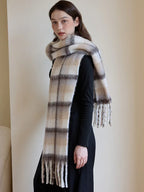 Profile view of a woman wearing a black top and pants, with a voluminous plaid scarf draped over her shoulders and neck.