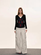 Woman posing in a black argyle v-neck sweater and light-colored cargo pants against a neutral background.