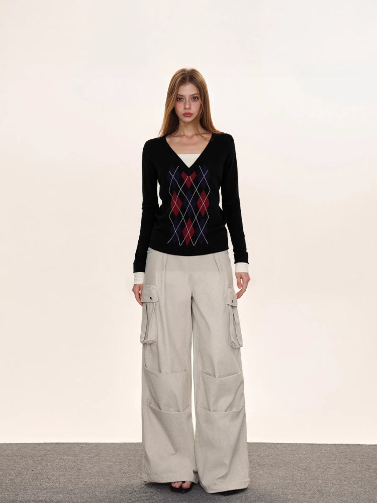 Woman posing in a black argyle v-neck sweater and light-colored cargo pants against a neutral background.