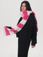 Model adjusting a pink and white striped fuzzy scarf worn with a black sweater and black dress.