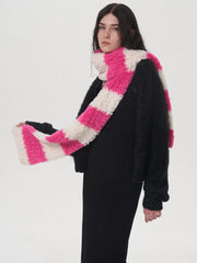 Model adjusting a pink and white striped fuzzy scarf worn with a black sweater and black dress.