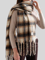 Front view of a woman wearing a large plaid scarf wrapped around her neck, with the fringe hanging down.