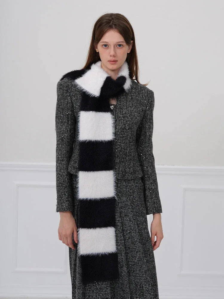 Woman wearing a black and white checkered faux fur scarf over a grey tweed jacket and skirt