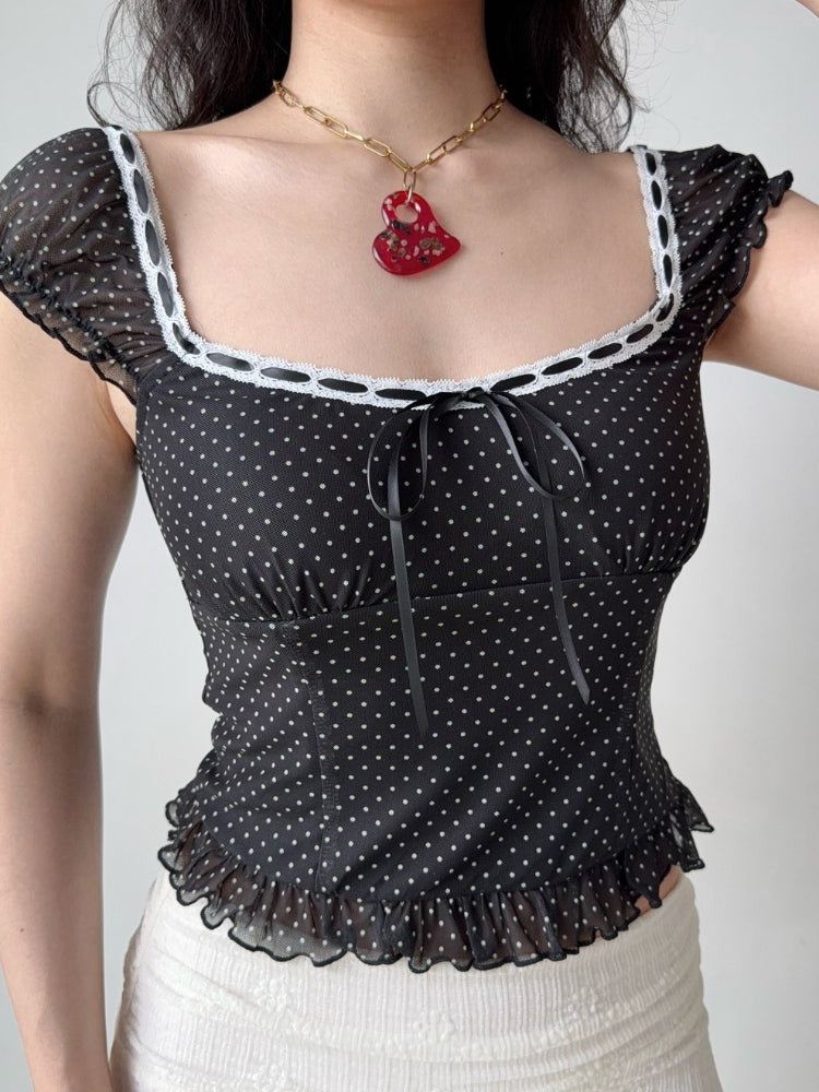 Front view of a woman wearing a black and white polka dot mesh top with a square neckline and tie front.
