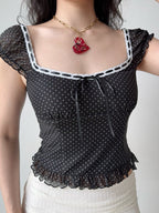Front view of a woman wearing a black and white polka dot mesh top with a square neckline and tie front.