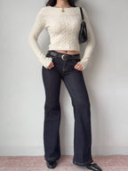 Full body shot of a model wearing a cream cable knit cropped sweater, dark wash flared jeans, and black loafers.