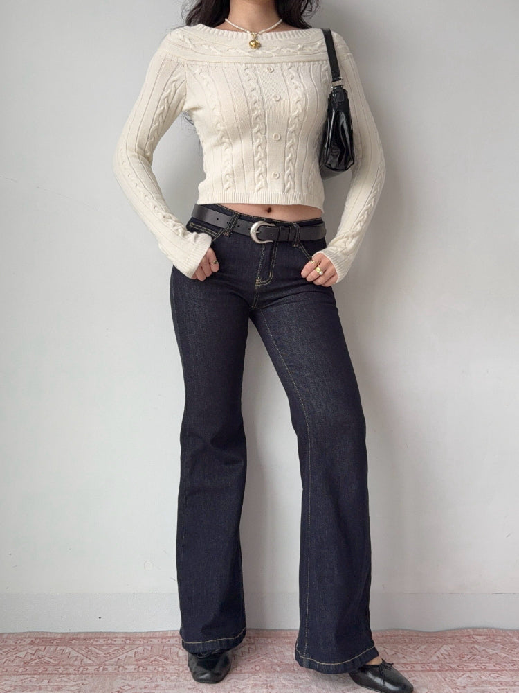 Full body shot of a model wearing a cream cable knit cropped sweater, dark wash flared jeans, and black loafers.
