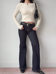 Full body shot of a model wearing a cream cable knit cropped sweater, dark wash flared jeans, and black loafers.