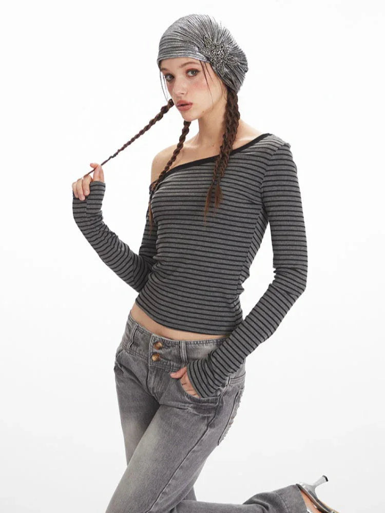 Woman posing in a grey and black striped off-the-shoulder long-sleeve top and grey wide-leg jeans.