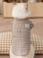 Rear view of a white cat wearing a brown plaid vest with ruffled sleeves.