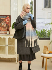 Woman wearing a charcoal gray coat, a light blue pair of gloves, and a large ombre scarf with pink, blue, and cream colors. The scarf has a fringed hem.