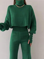 Woman wearing a green knit two-piece set with a cropped turtleneck sweater and wide leg pants, accessorized with a gold necklace.