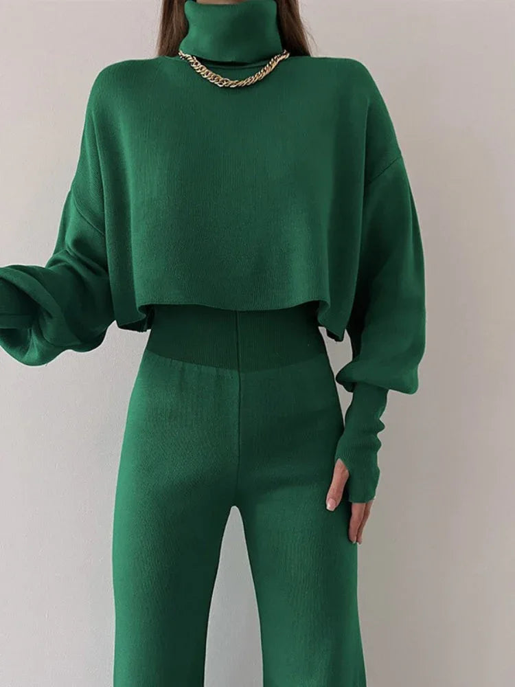 Woman wearing a green knit two-piece set with a cropped turtleneck sweater and wide leg pants, accessorized with a gold necklace.