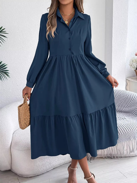 Woman standing wearing a long-sleeved blue midi dress with a collared neckline and tiered hem
