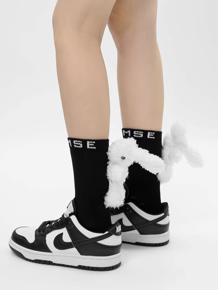 Side view of black ankle socks with white 3D plush bunny embellishments and white sneakers