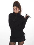Close-up of a woman wearing a black turtleneck sweater with fringe details on the sleeves.