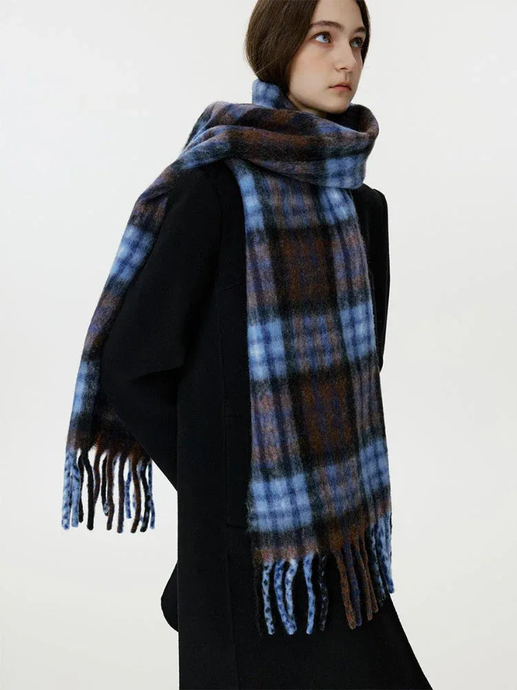 Woman wearing a black coat and a large blue and brown plaid scarf with fringe detail.