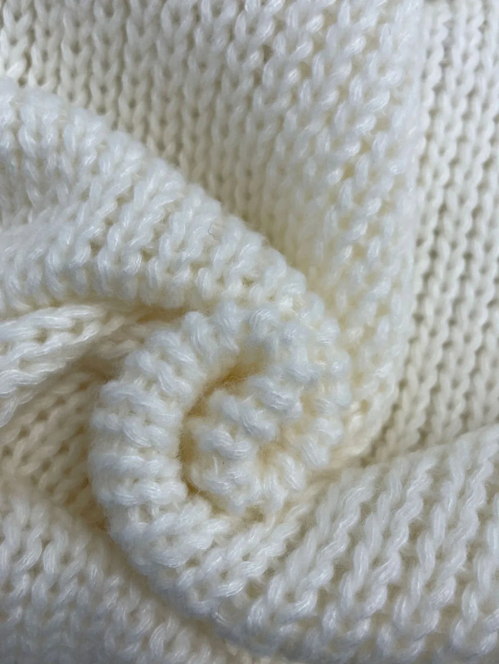 Detailed texture of the cream chunky knit fabric of the sweater.