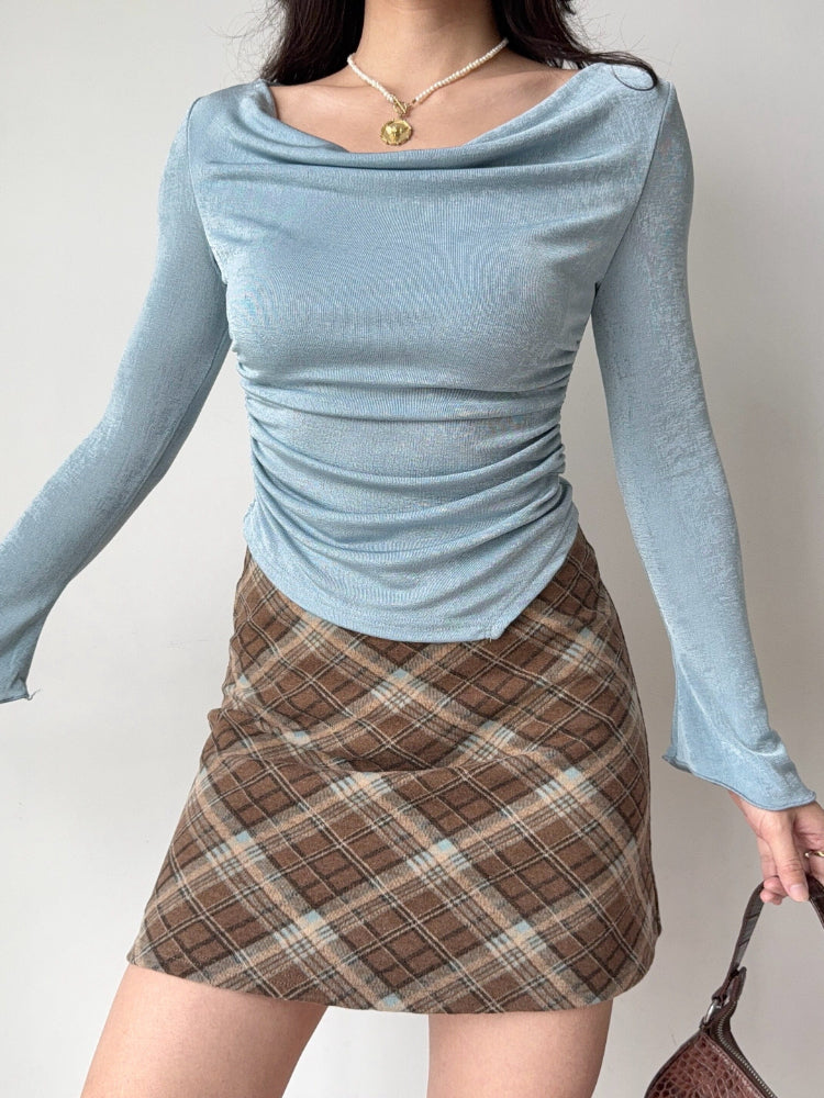 Woman wearing a light blue long-sleeved top with a cowl neckline and ruched side detailing.