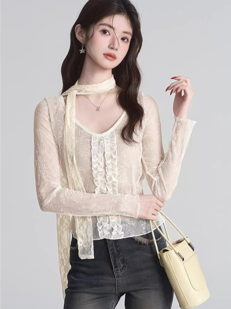 A woman models a cream-colored lace top with a v-neck and a scarf detail, paired with dark denim jeans.