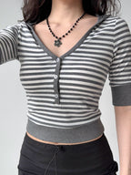 Front view of a woman wearing a grey and white striped cropped top with a v-neck and button front.