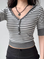 Front view of a woman wearing a grey and white striped cropped top with a v-neck and button front.