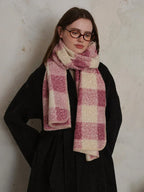 Woman wearing a black coat and a pink and cream plaid scarf, looking down.