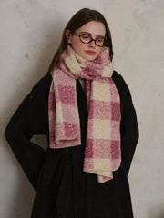 Woman wearing a black coat and a pink and cream plaid scarf, looking down.