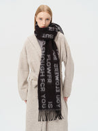 Woman wearing a black scarf with white text and a beige cardigan