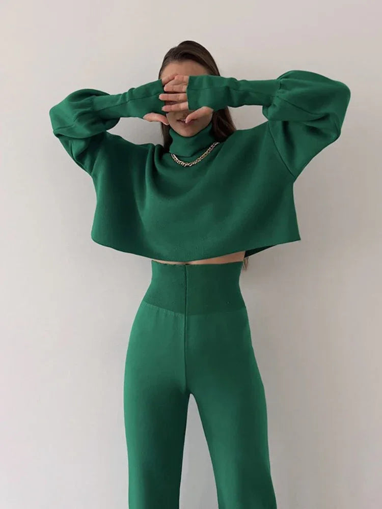 Front view of a woman in a green knit two-piece set, showing the cropped turtleneck sweater and high-waisted wide leg pants.