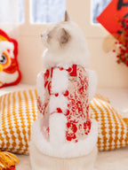 The back of a white cat wearing a red traditional Chinese jacket with floral patterns and faux fur trim, sitting on a cushion.