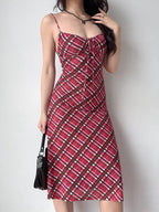 A woman adjusts her hair while wearing a red plaid midi dress with spaghetti straps and a black handbag.