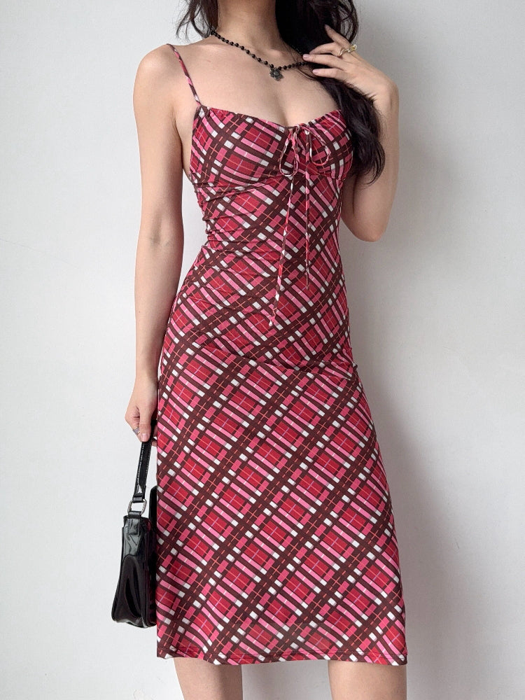 A woman adjusts her hair while wearing a red plaid midi dress with spaghetti straps and a black handbag.