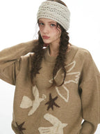 Close-up of the front of a woman's brown knit sweater featuring a bird and star motif.