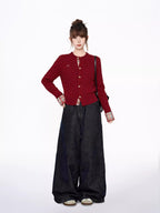 Full body shot of a woman in a red cable knit cardigan, plaid shirt, and wide-leg jeans, with hands on hips.