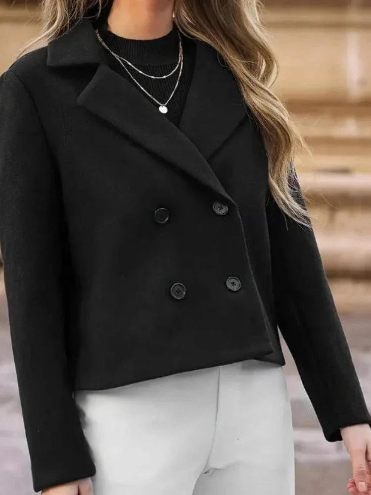 Model showcasing a black double-breasted cropped jacket over a black top and white pants