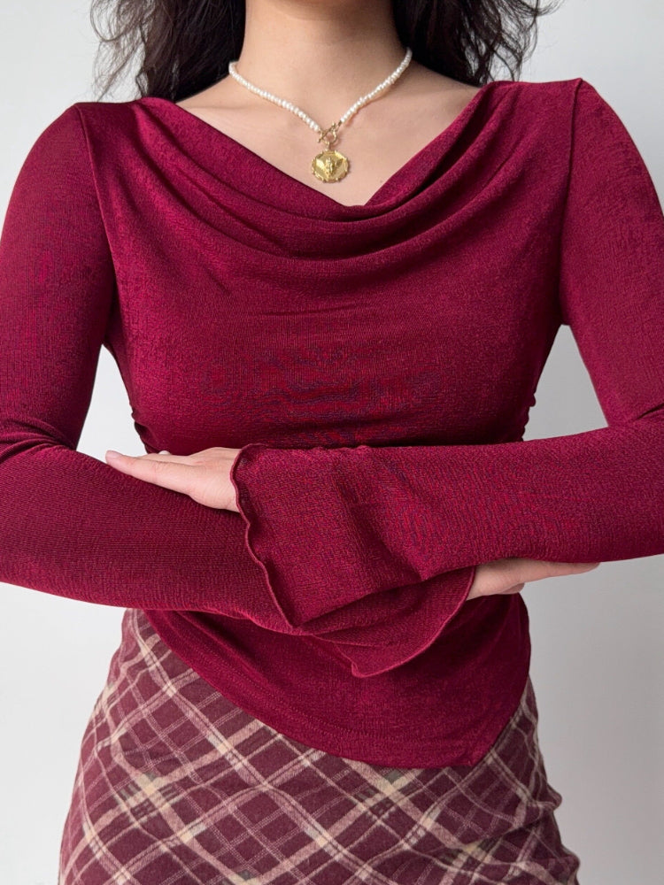 Close-up of a woman wearing a burgundy long-sleeved top with a cowl neckline and ruched detailing.