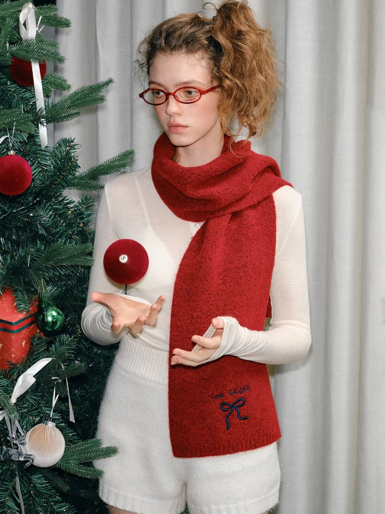 Woman in a red knit scarf holding a red ornament, with a Christmas tree in the background.